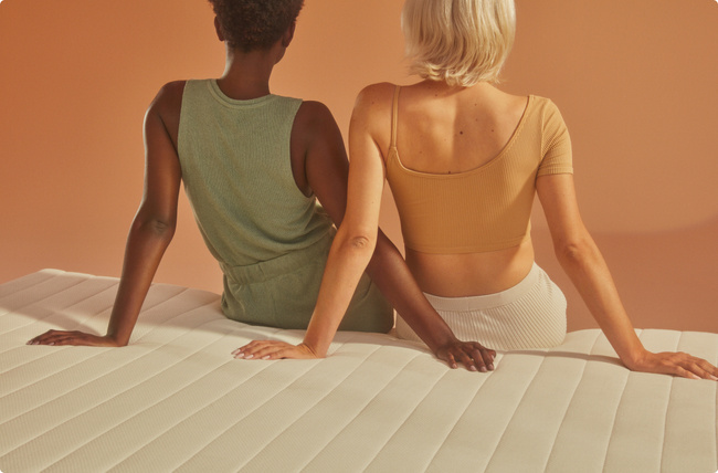 two people sitting on mattress with backs to viewer